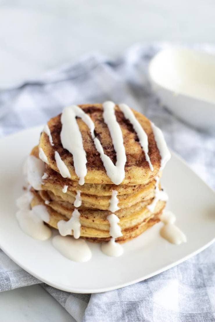 Keto cinnamon roll pancakes with cream on a white plate.