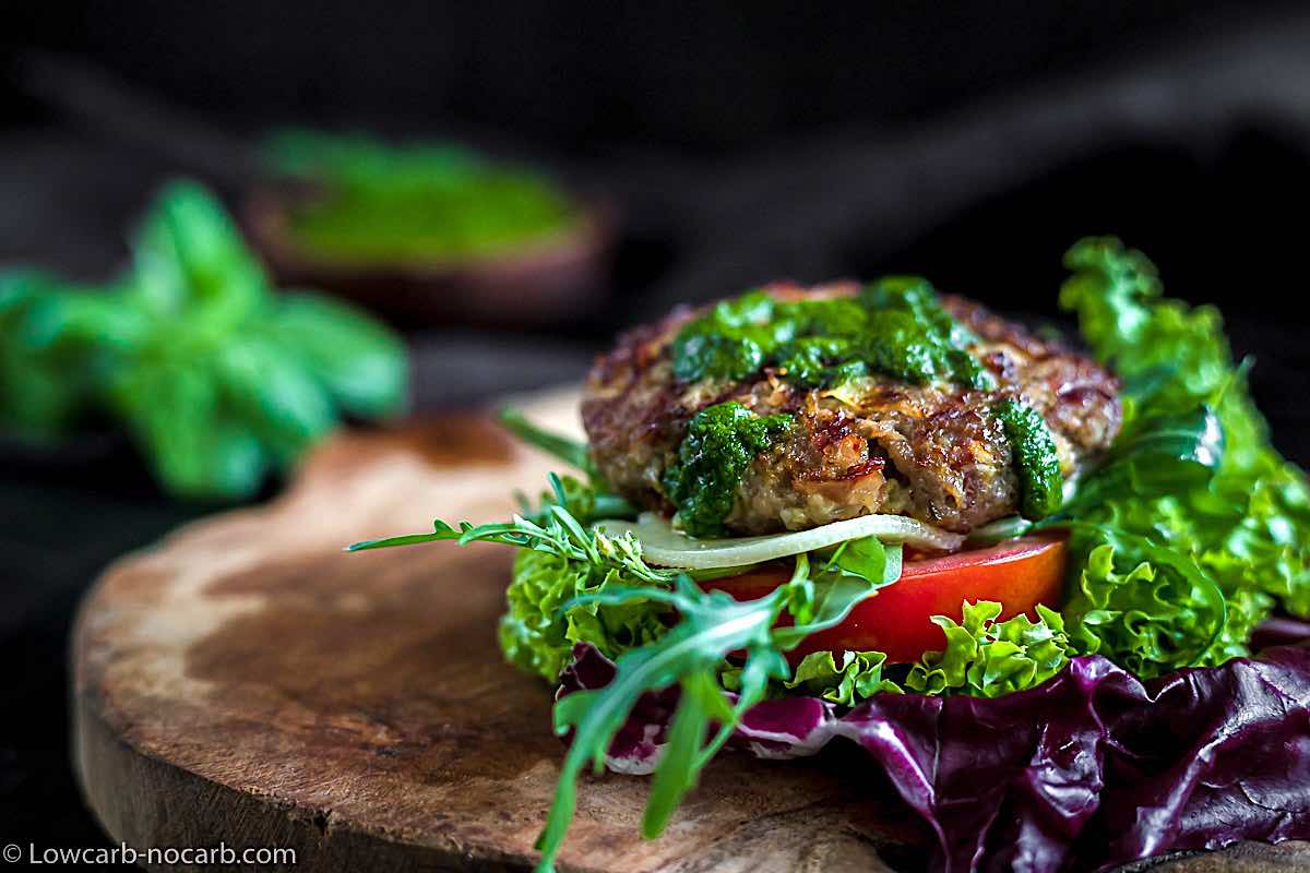 Keto ground beef burger with vegetables on a wooden board.
