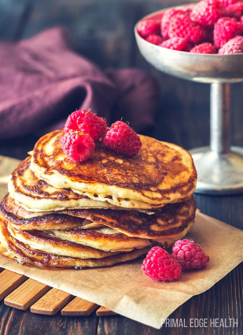 A stack of pancakes with raspberries on a wooden surface.