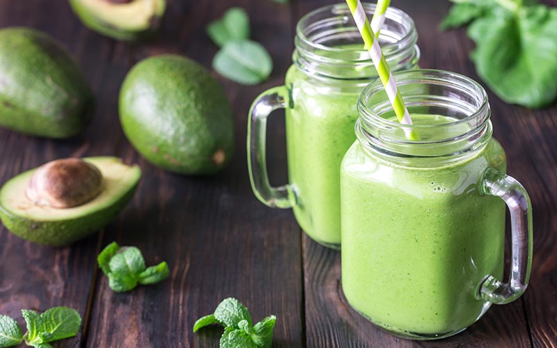 Two glasses of green smoothie garnished with avocado.