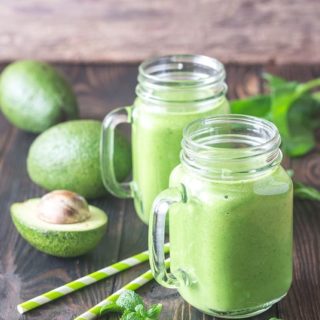 Two servings of green smoothie in a glass with two green straws.