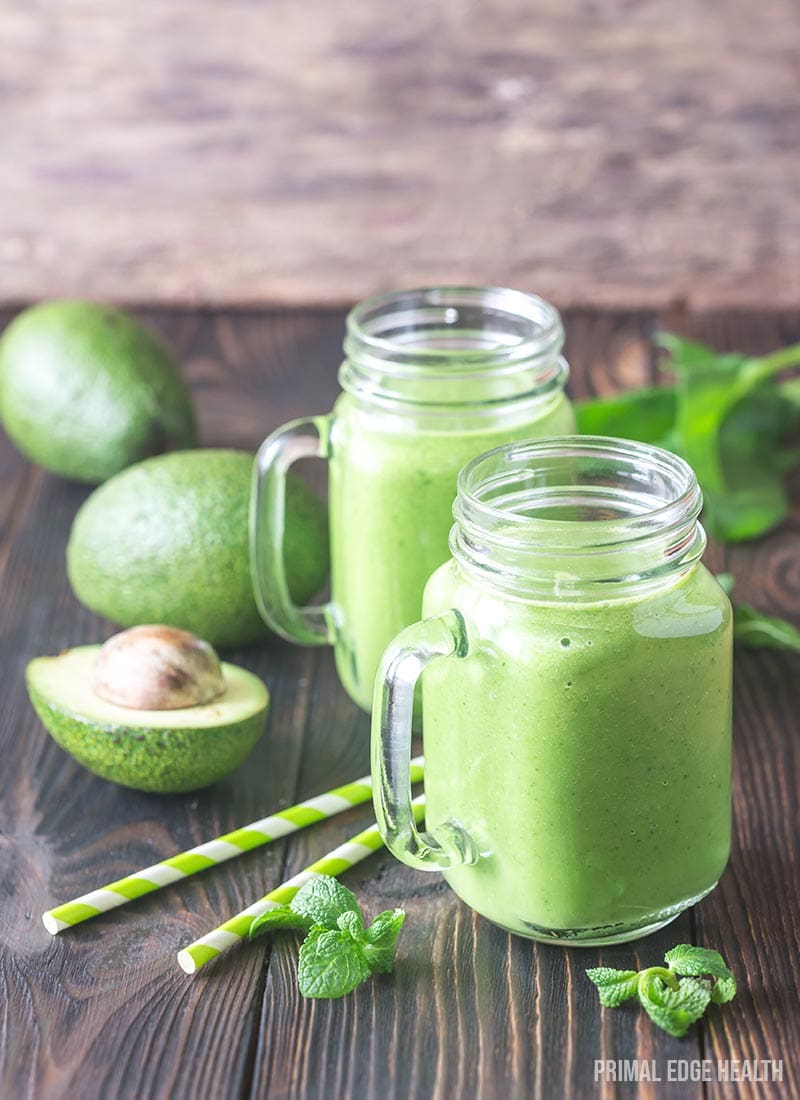 Two servings of green smoothie in a glass with two green straws.