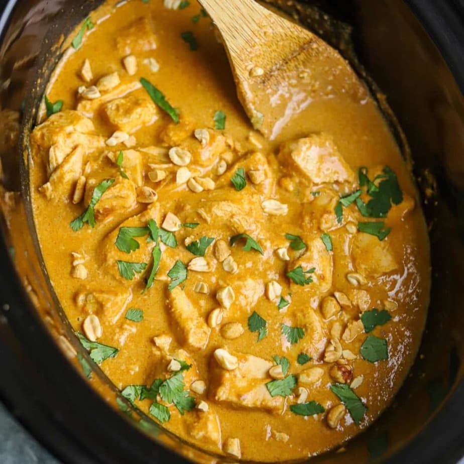 Slow Cooker Thai Peanut Chicken in a black pot with a wooden spoon.