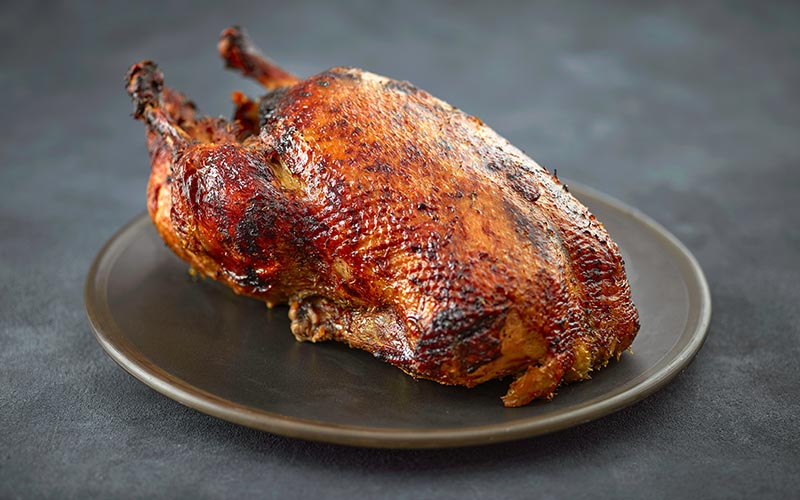 A whole cooked chicken on a plate on a grey surface.