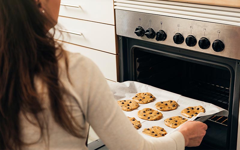 A woman putting a batch of unbaked cookies into the oven.