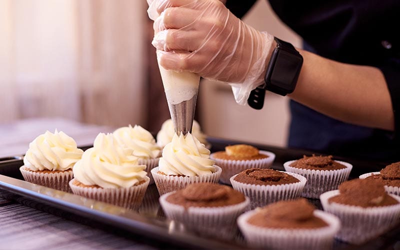 A person putting icing on a batch of cupcakes.