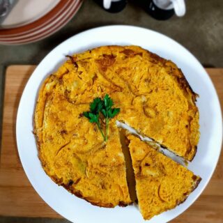 Spanish omelette one a white plate over a wooden board.