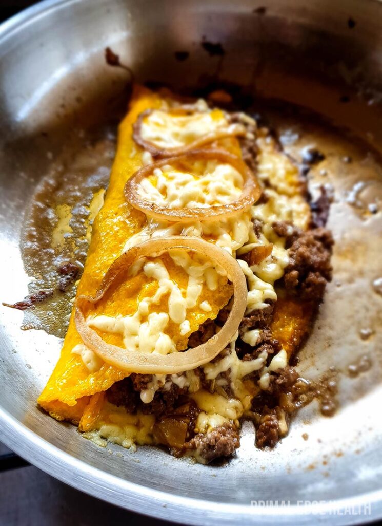 Cheeseburger carnivore omelette on a pan garnished with onions.