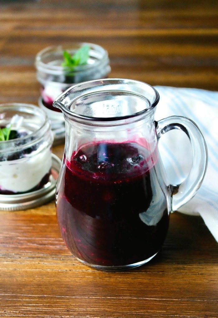 Blueberry sauce in a small glass container on a wooden surface.