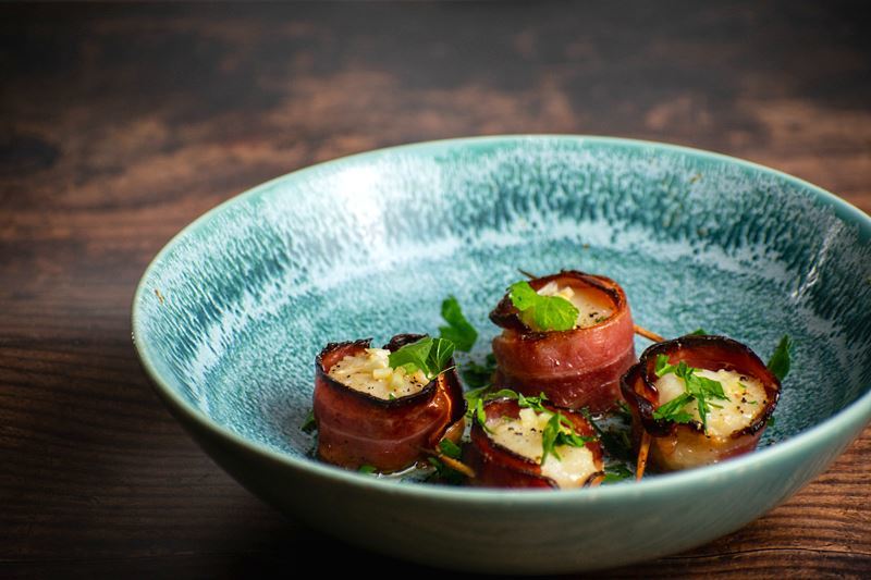 Scallops wrapped in bacon in a blue bowl.