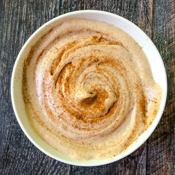 Cashew cheese cinnamon in a white bowl on a wooden surface.