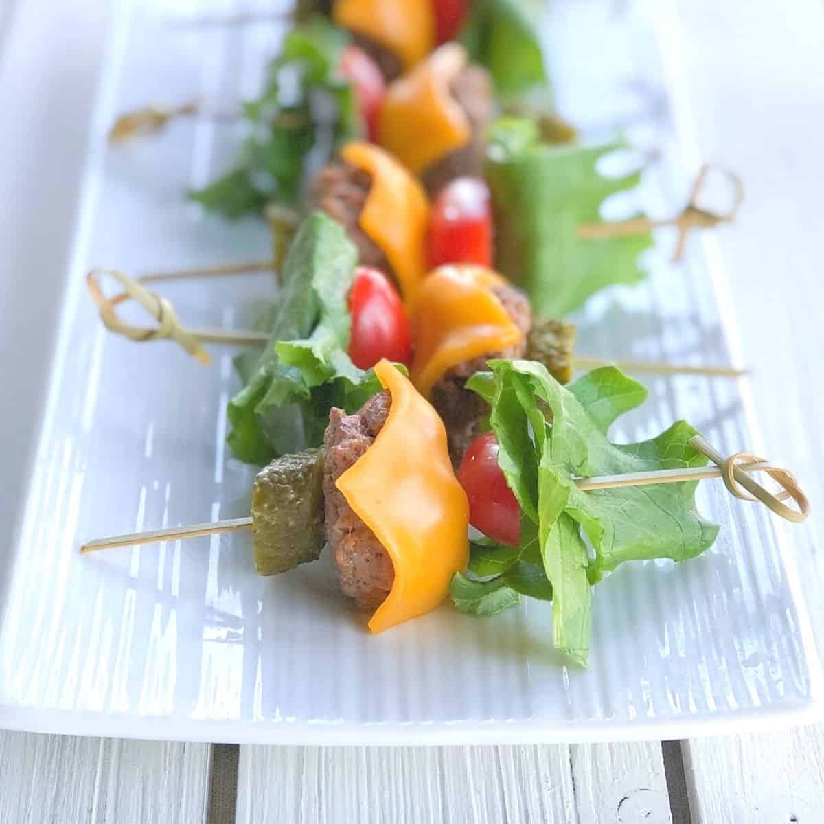 Mini cheeseburger skewers on a white long plate.