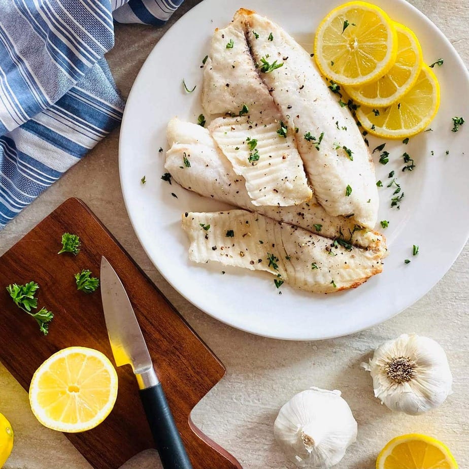 Slices of fish and lemon on a white plate garnished.