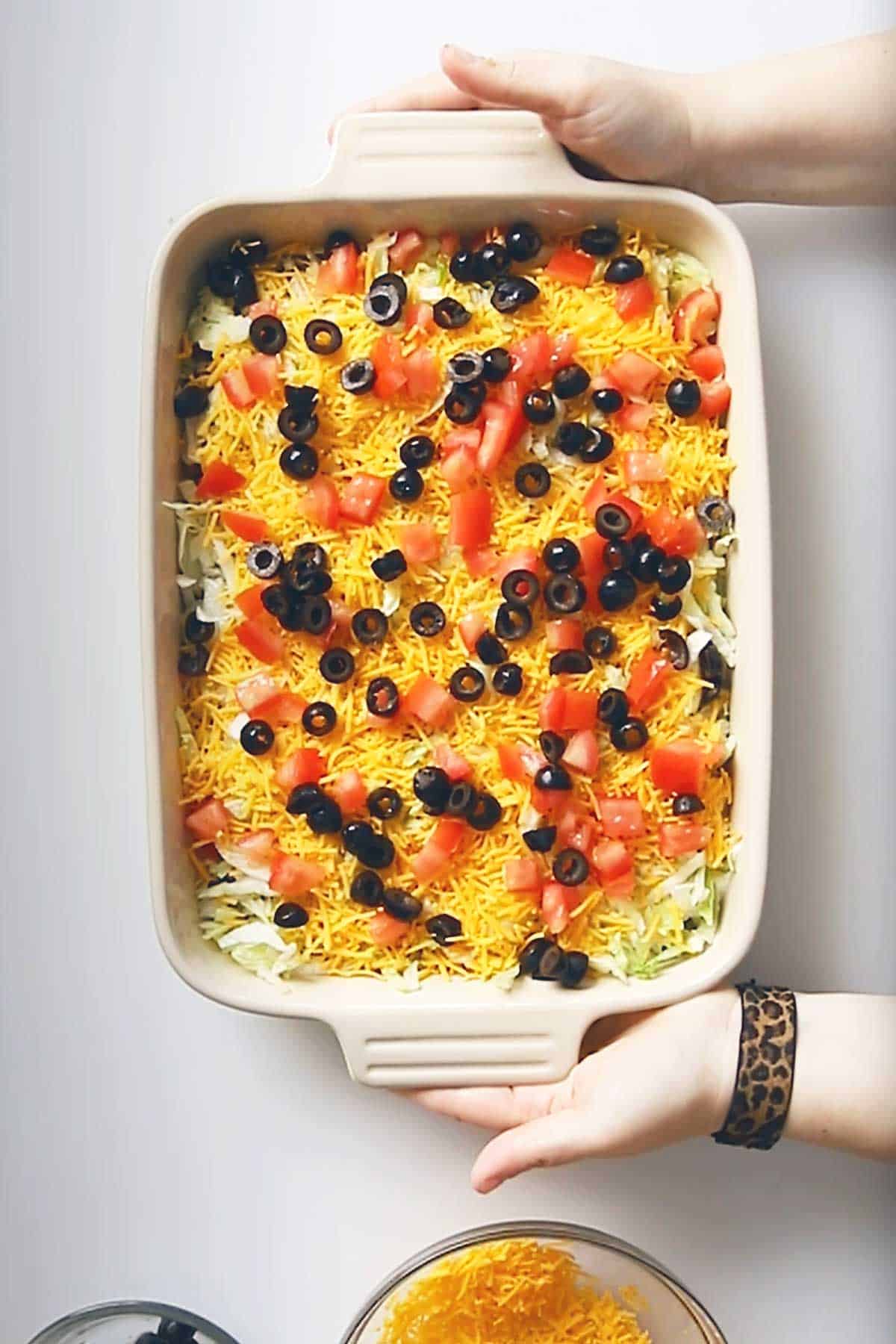 keto 7 layer dip in a white dish held by a person's hands.
