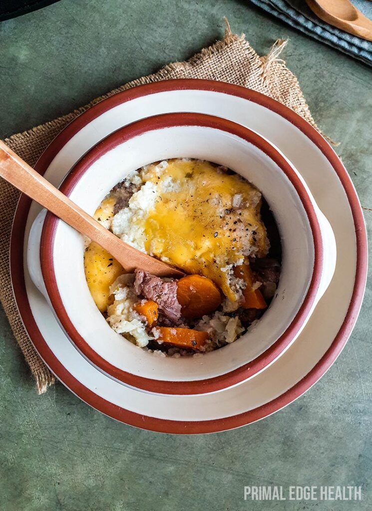 Keto shepherd's pie in a white bowl served with a wooden spoon.