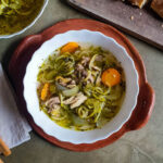 A bowl of keto chicken noodle soup served with bread on a tray.