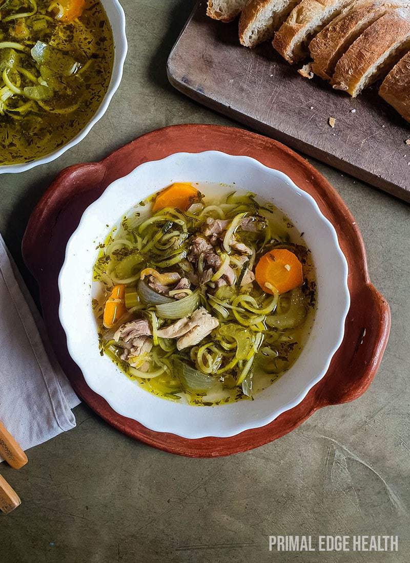 A bowl of keto chicken noodle soup served with bread on a tray.