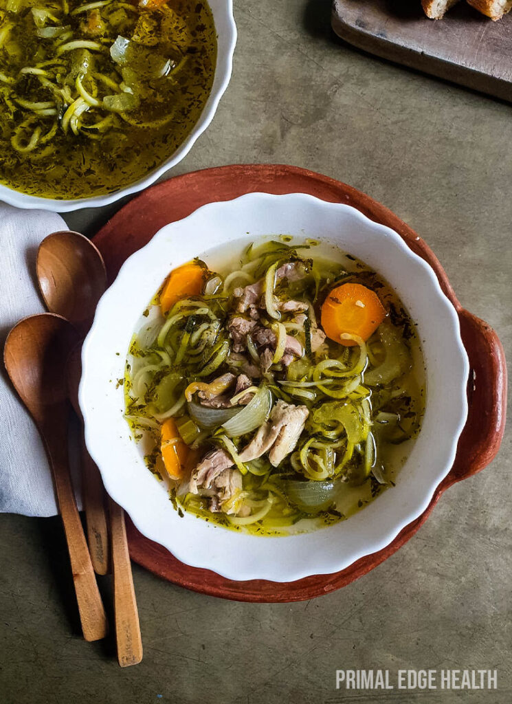 Keto chicken noodle soup in a bowl on a grey surface.