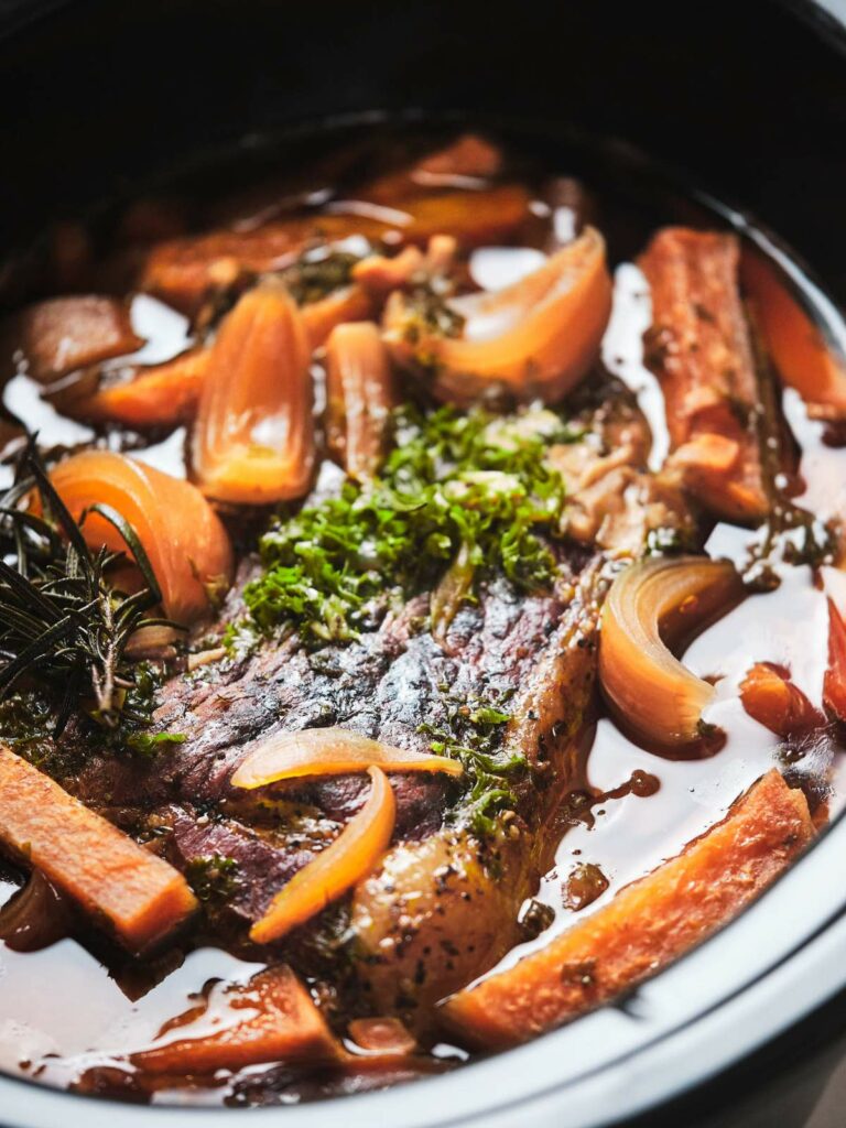 Slow-cooked pot roast with carrots and herbs in a black pot.