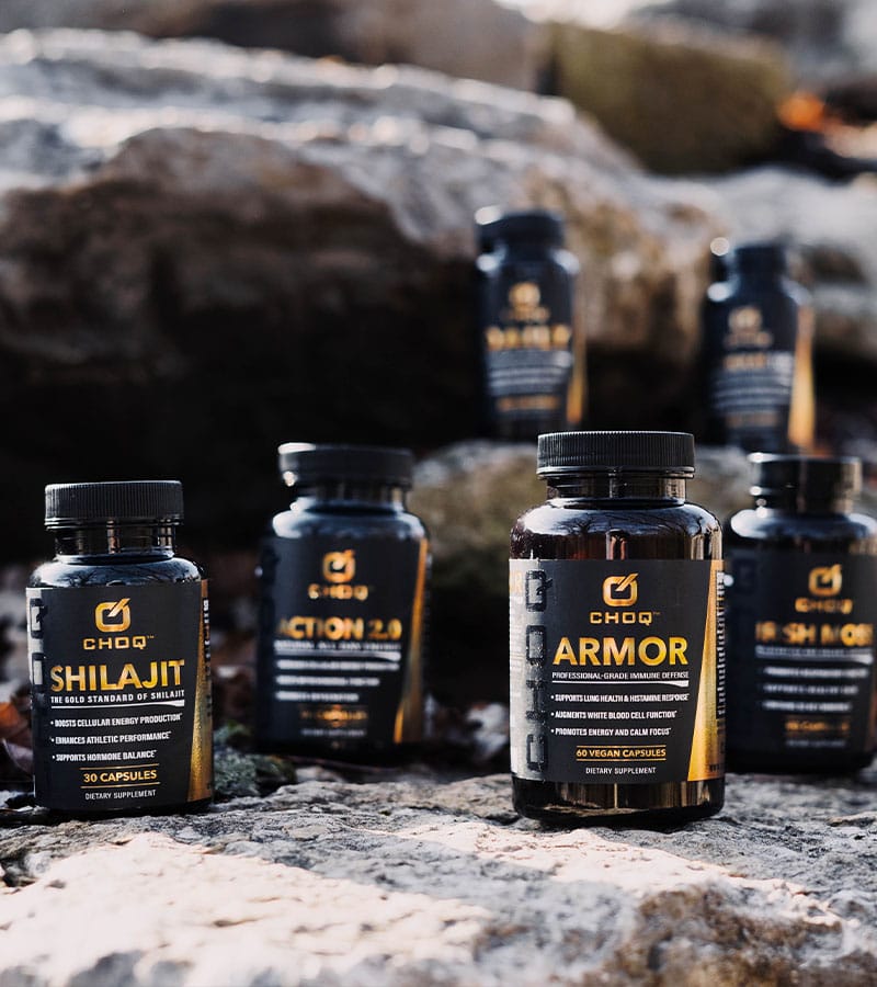 6 bottles of Choq Shilajit supplement on a rocky surface.