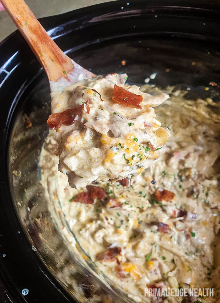 A wooden spoon stirring healthy crack chicken in a crock pot.