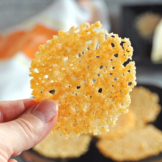 A person's hand holding up a piece of baked parmesan crisp.