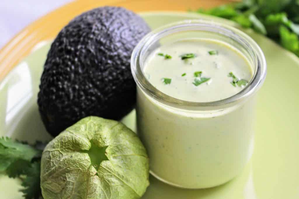 A glass of homemade avocado dressing on a green plate.