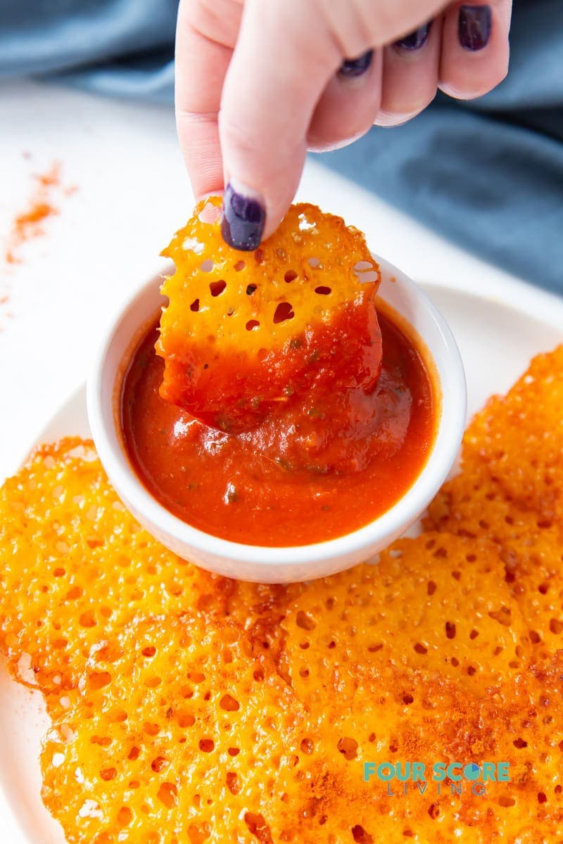 Keto cheese chip being dipped in a red sauce.