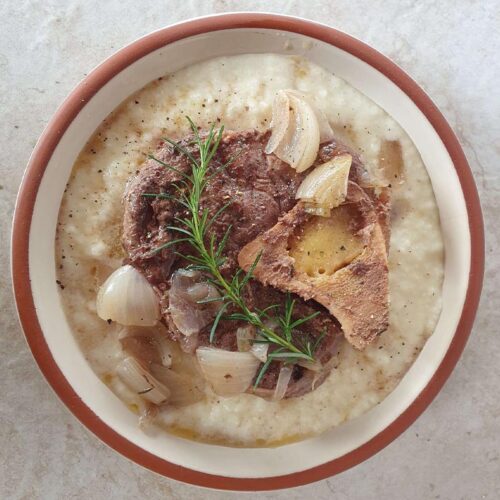 Beef shank cross cut with garnish in a bowl on a white surface.