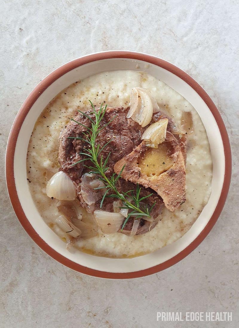 Beef shank cross cut with garnish in a bowl on a white surface.