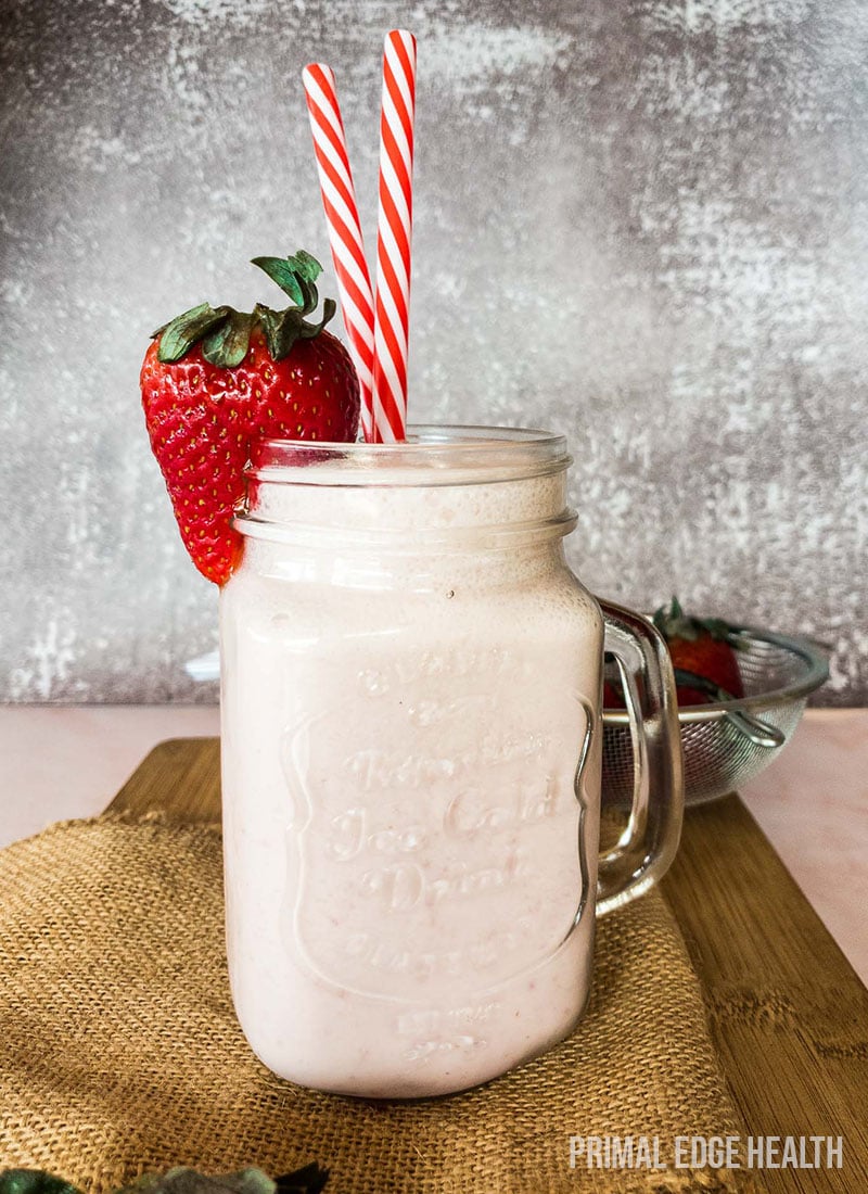 A glass of strawberry cheesecake smoothie served on a wooden board.