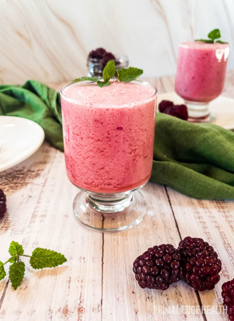 A pink smoothie surrounded by blackberries and a green cloth.