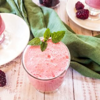 A glass of blackberry smoothie with garnish on a wooden surface.