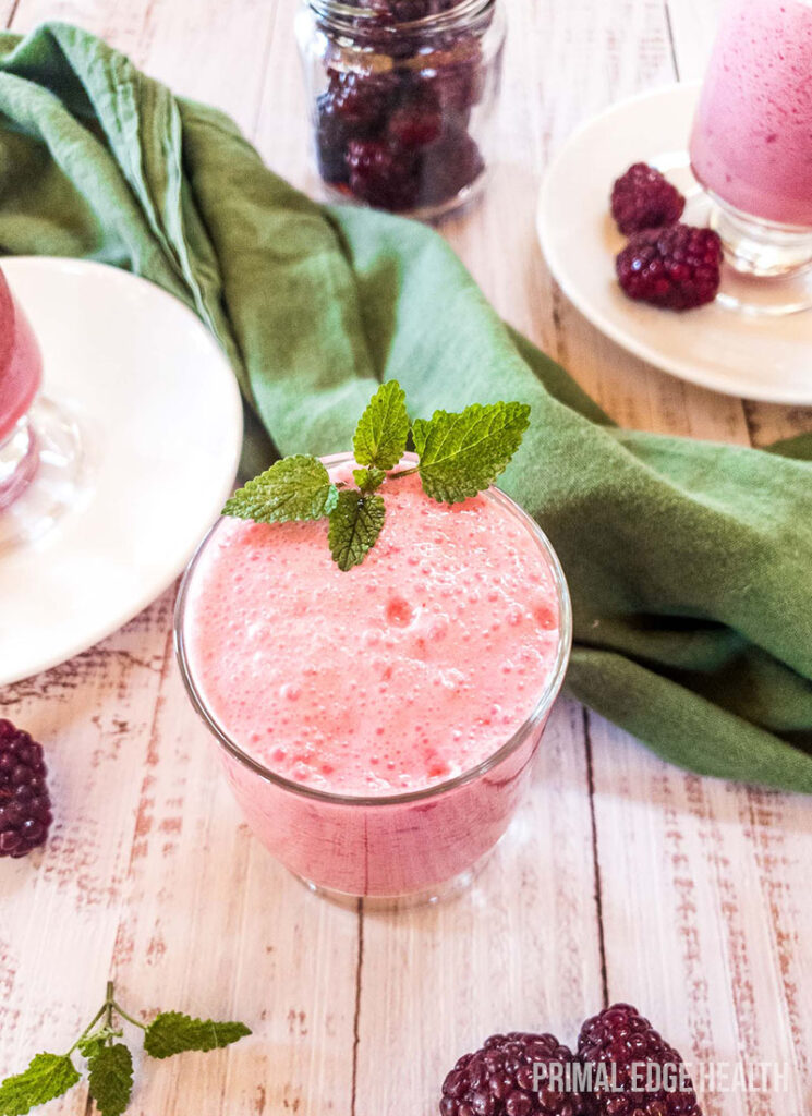 A glass of blackberry smoothie with garnish on a wooden surface.