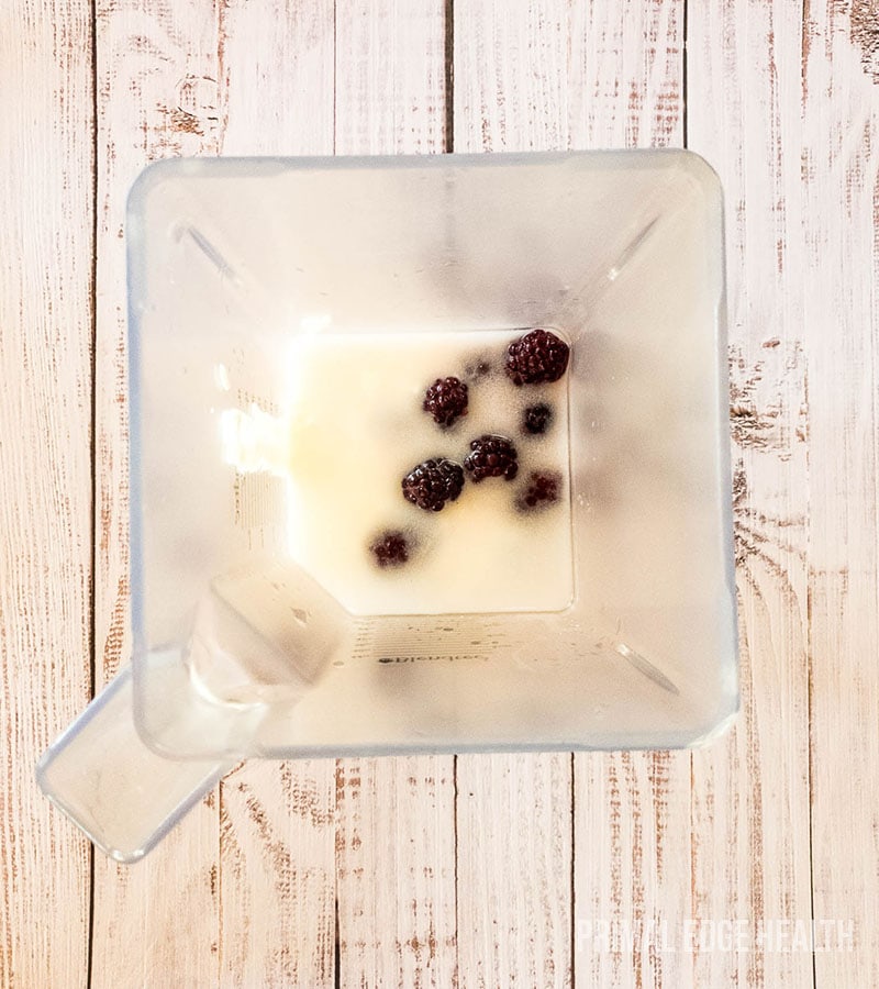 A white creamy liquid with blackberries in a container.