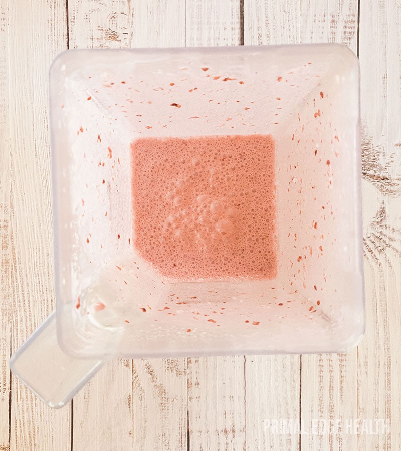 A frothy pink liquid in a container on a wooden surface.