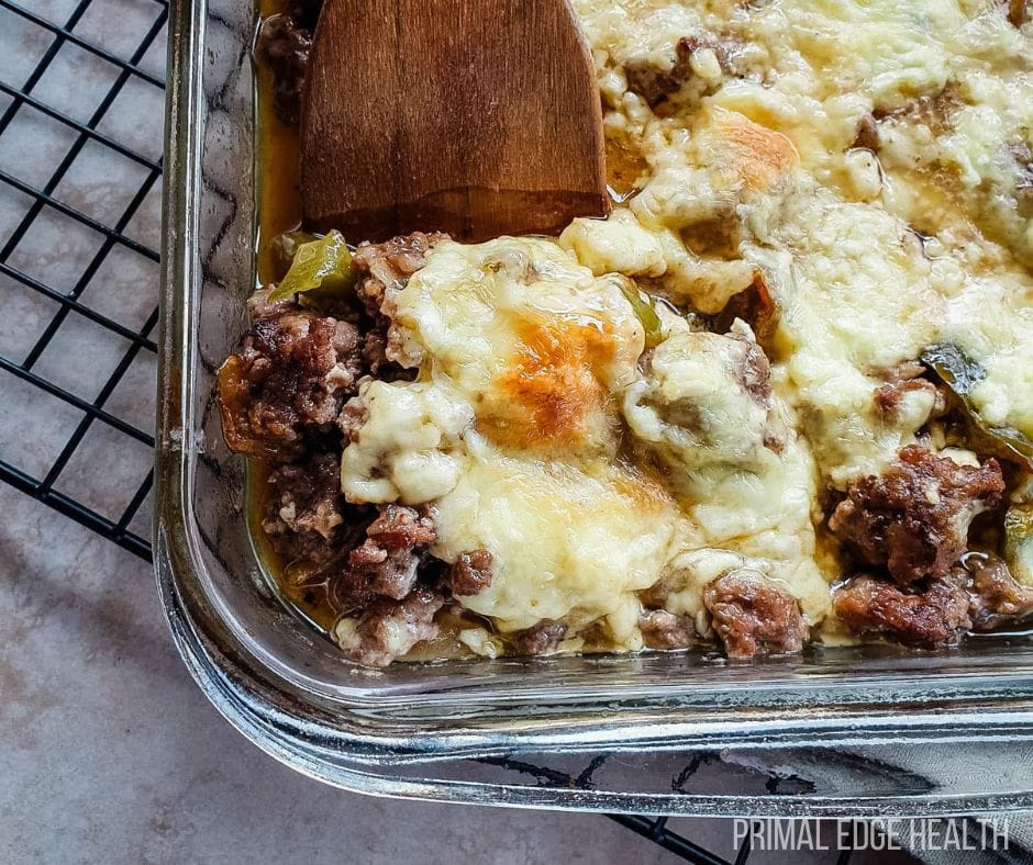 A glass dish of philly cheesesteak casserole with a wooden spatula.