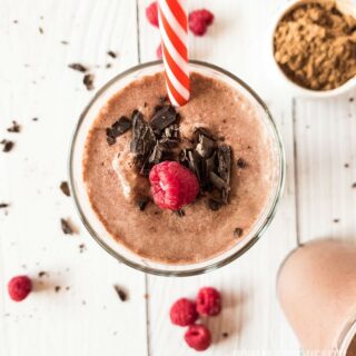 Glass of brown smoothie garnished with raspberry and chocolate.