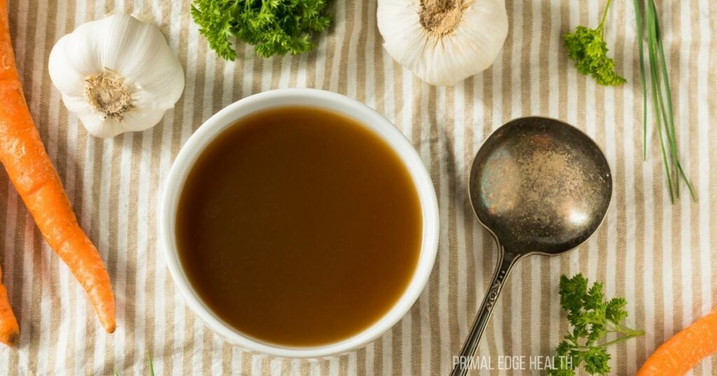 A serving of broth in a small white bowl surrounded by garnishes.