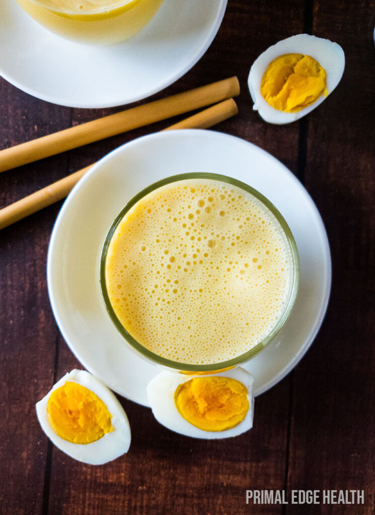 A glass of egg smoothie on a wooden surface.
