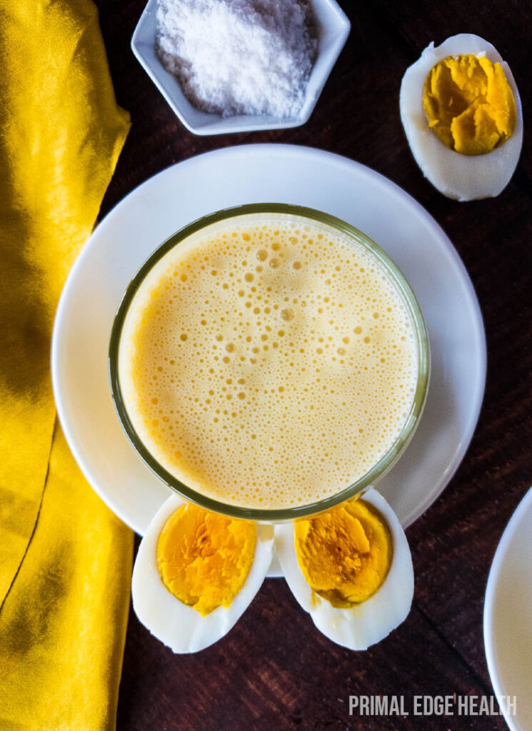 A glass of egg smoothie on a wooden surface with yellow cloth.