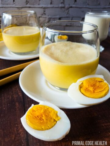 Egg smoothie in a glass on white saucer plate.