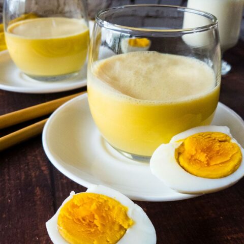 Egg smoothie in a glass on white saucer plate.