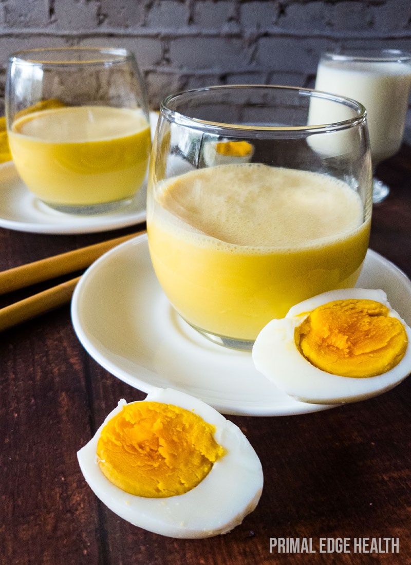 Egg smoothie in a glass on white saucer plate.