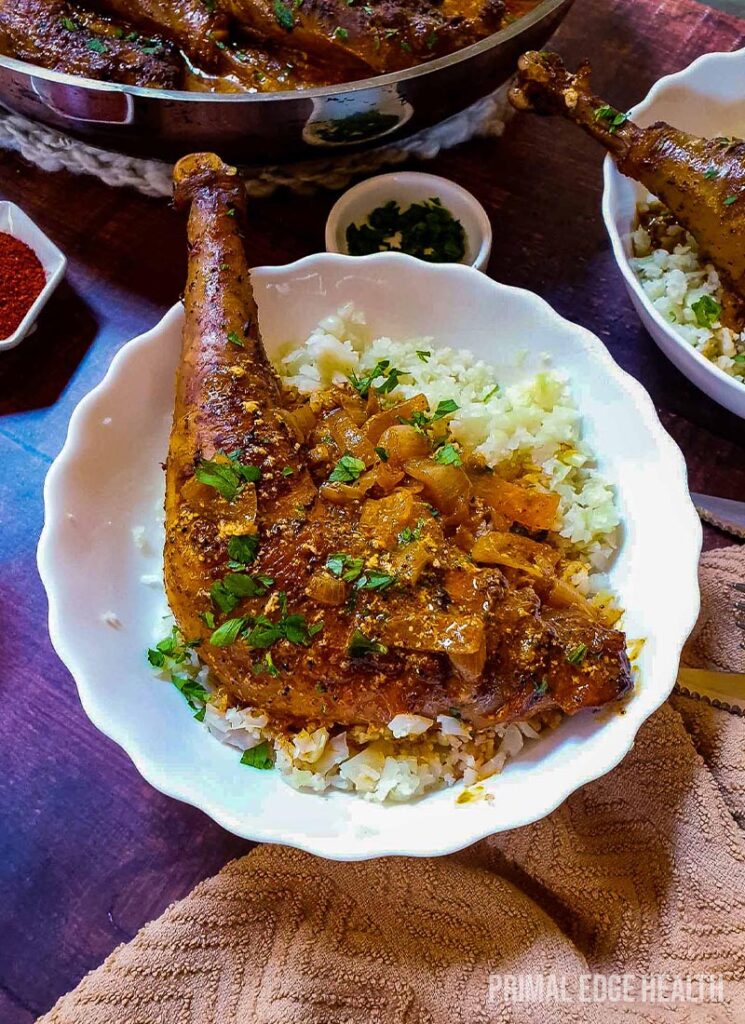 Keto chicken leg served over rice garnished with herbs on a white bowl.