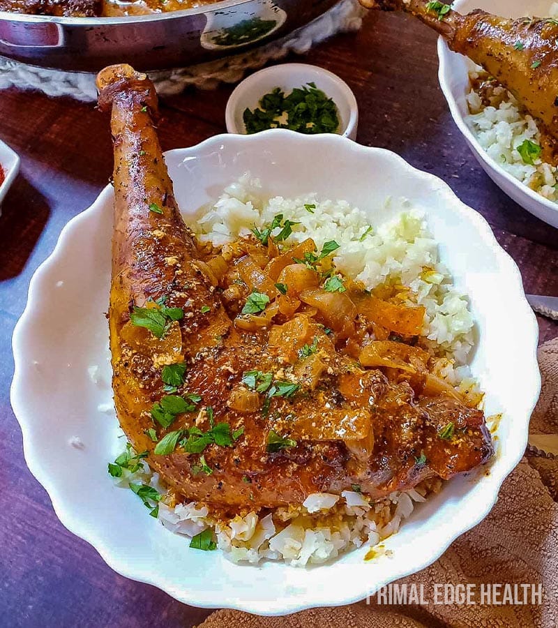 A seasoned keto chicken leg served over rice, garnished with fresh herbs.