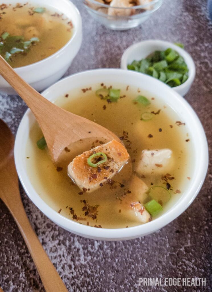 A bowl of soup with a piece of meat and chopped green onions.