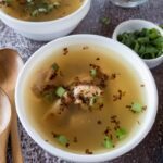 Two bowls of soup garnished with herbs on a textured surface.