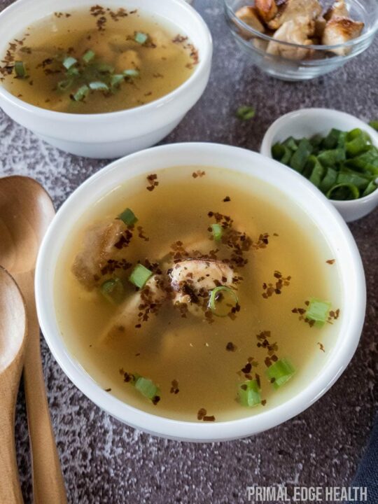 Two bowls of soup garnished with herbs on a textured surface.