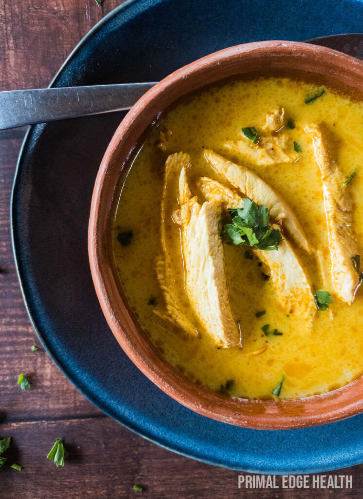 Yellow soup served with spoon in a bowl.